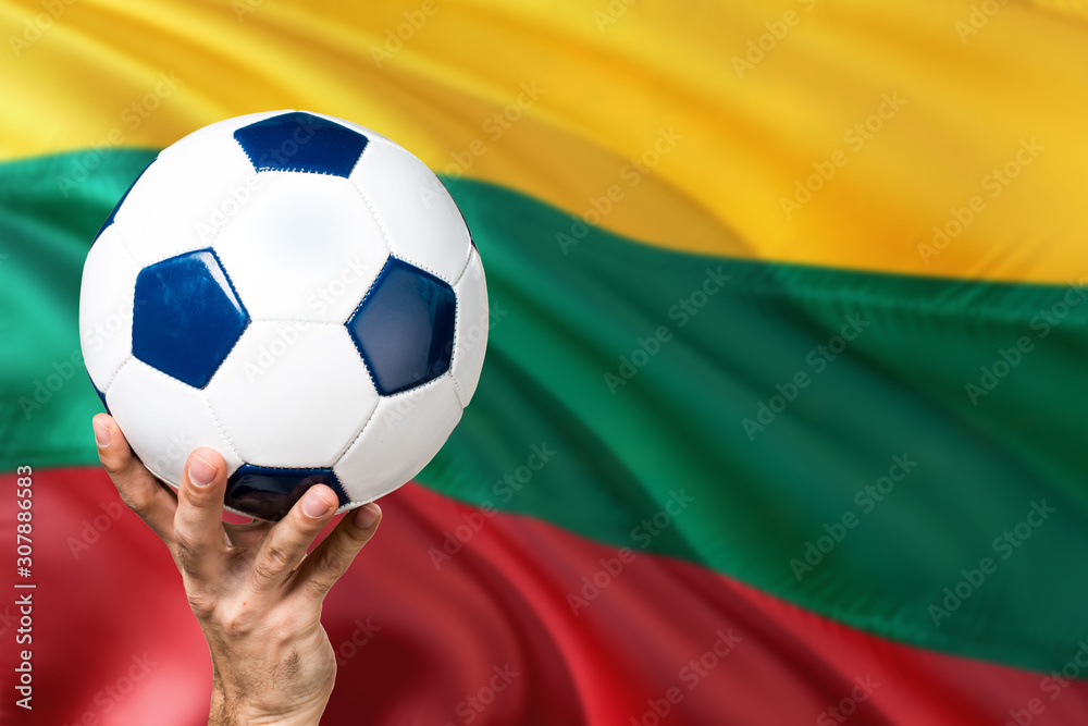Naklejka premium Lithuania soccer concept. National team player hand holding soccer ball with country flag background. Copy space for text.