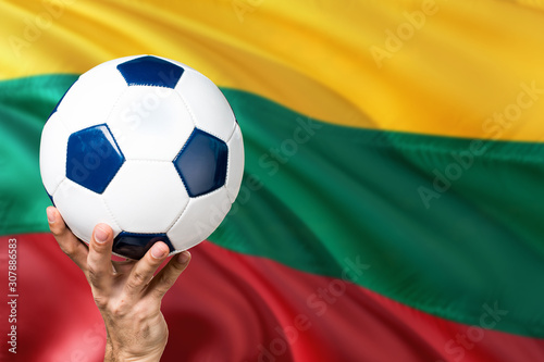 Lithuania soccer concept. National team player hand holding soccer ball with country flag background. Copy space for text.