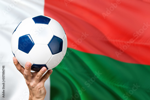 Madagascar soccer concept. National team player hand holding soccer ball with country flag background. Copy space for text.