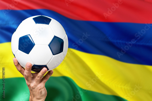 Mauritius soccer concept. National team player hand holding soccer ball with country flag background. Copy space for text.