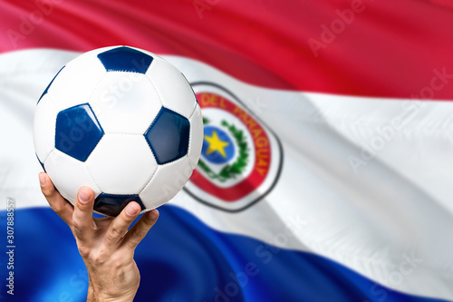 Paraguay soccer concept. National team player hand holding soccer ball with country flag background. Copy space for text.