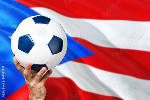 Puerto Rico soccer concept. National team player hand holding soccer ball with country flag background. Copy space for text.