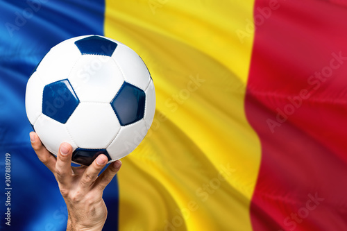 Romania soccer concept. National team player hand holding soccer ball with country flag background. Copy space for text.