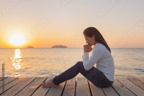 The girl sits in prayer to God with a promise. With love for God At sea ocean Outdoors during the sunset in the winter