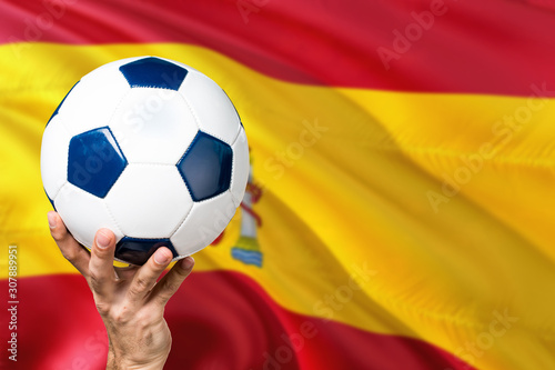 Spain soccer concept. National team player hand holding soccer ball with country flag background. Copy space for text.