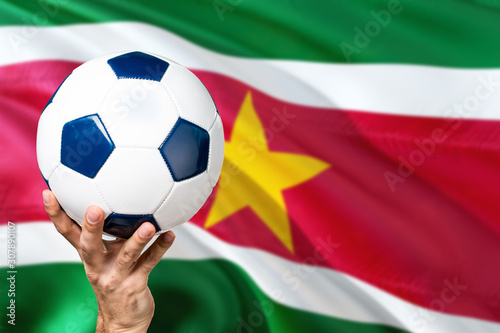 Suriname soccer concept. National team player hand holding soccer ball with country flag background. Copy space for text.