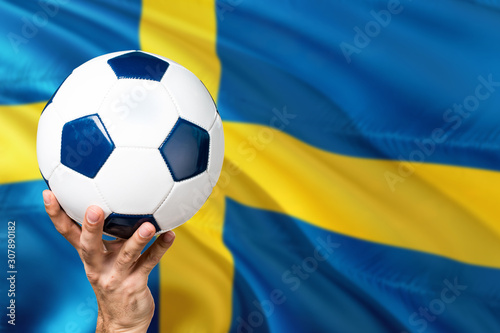 Sweden soccer concept. National team player hand holding soccer ball with country flag background. Copy space for text.