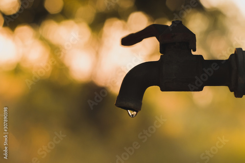 Water dripping from the faucet and the yellow bokeh background in evening (silhouette).