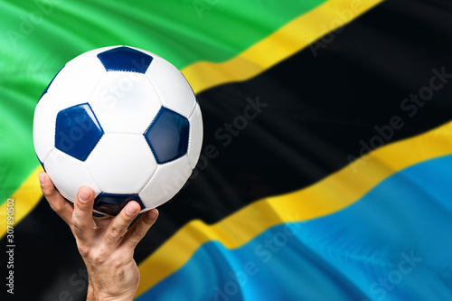 Tanzania soccer concept. National team player hand holding soccer ball with country flag background. Copy space for text.