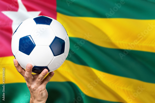 Togo soccer concept. National team player hand holding soccer ball with country flag background. Copy space for text.