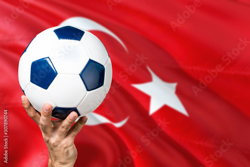 Turkey soccer concept. National team player hand holding soccer ball with country flag background. Copy space for text.