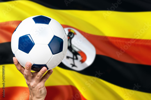 Uganda soccer concept. National team player hand holding soccer ball with country flag background. Copy space for text.