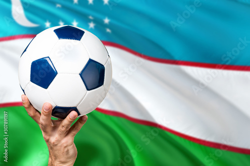 Uzbekistan soccer concept. National team player hand holding soccer ball with country flag background. Copy space for text.