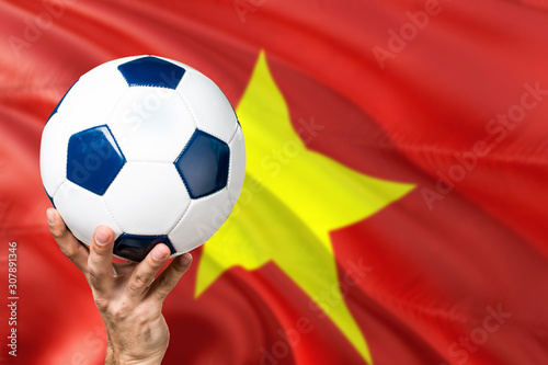 Vietnam soccer concept. National team player hand holding soccer ball with country flag background. Copy space for text.