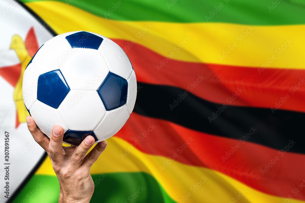 Zimbabwe soccer concept. National team player hand holding soccer ball with country flag background. Copy space for text. Zimbabwe soccer concept. National team player hand holding soccer ball with country flag background. Copy space for text.