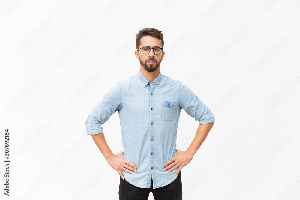 © Mangostar - Front of serious determined guy keeping hands on hip. Handsome young man in casual shirt and glasses standing isolated over white background. Male portrait concept © Mangostar - Front of serious determined guy keeping hands on hip. Handsome young man in casual shirt and glasses standing isolated over white background. Male portrait concept