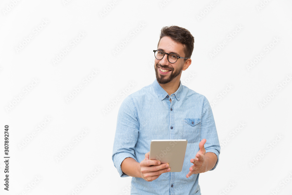 Happy joyful guy with tablet getting good news, looking at camera, smiling, gesturing. Handsome young man in casual shirt and glasses standing isolated over white background. Good news concept Happy joyful guy with tablet getting good news, looking at camera, smiling, gesturing. Handsome young man in casual shirt and glasses standing isolated over white background. Good news concept
