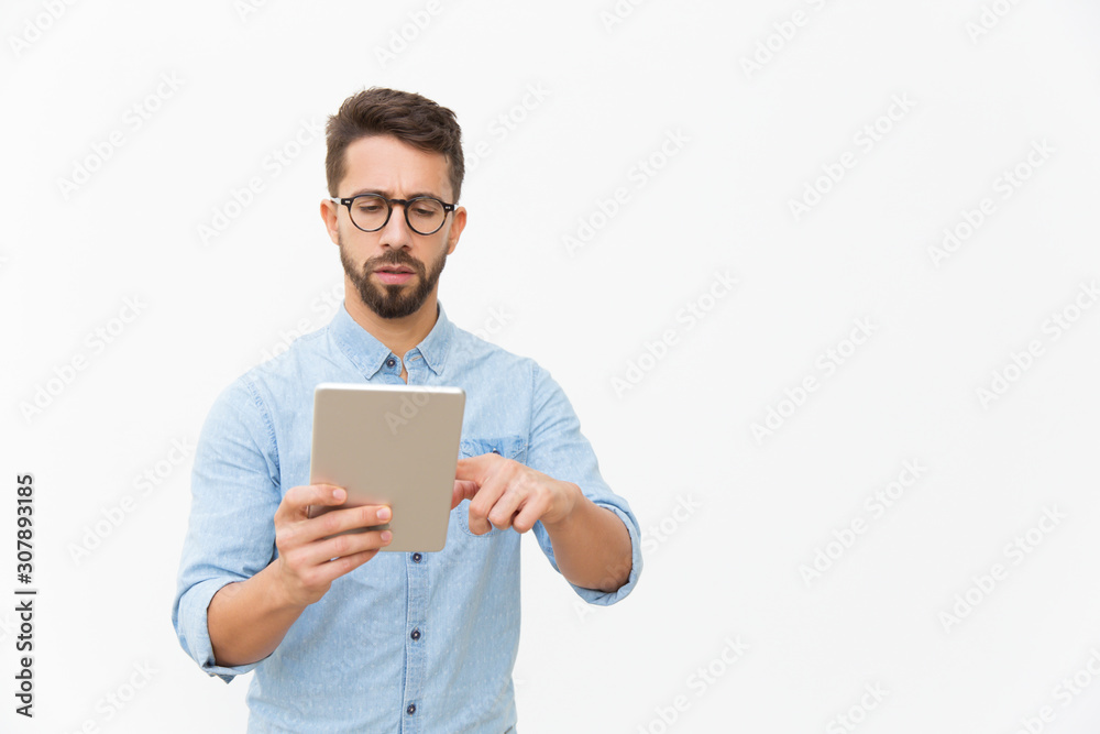 Focused professional working on tablet. Handsome young man in casual shirt and glasses standing isolated over white background. Digital communication concept