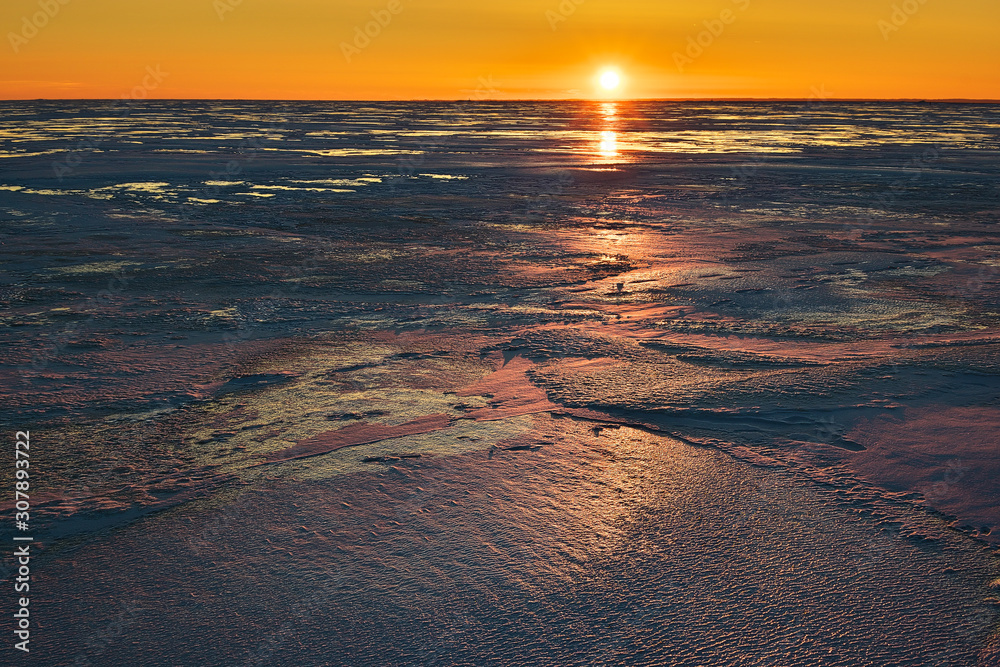 View to the fully frozen Baltic sea in Pärnu, Estonia colored by sunset in vivid colors on sunny and cold February evening, focus on ice in foreground