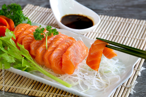 Salmon sashimi with vegetables in white dish and wasabi with Soyu sauce in white bowl all put on bamboo mat photo