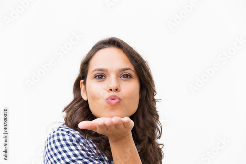 Cute cheerful Latin woman blowing kiss, expressing love or tenderness. Young woman in casual checked shirt standing isolated over white background. Air kiss concept