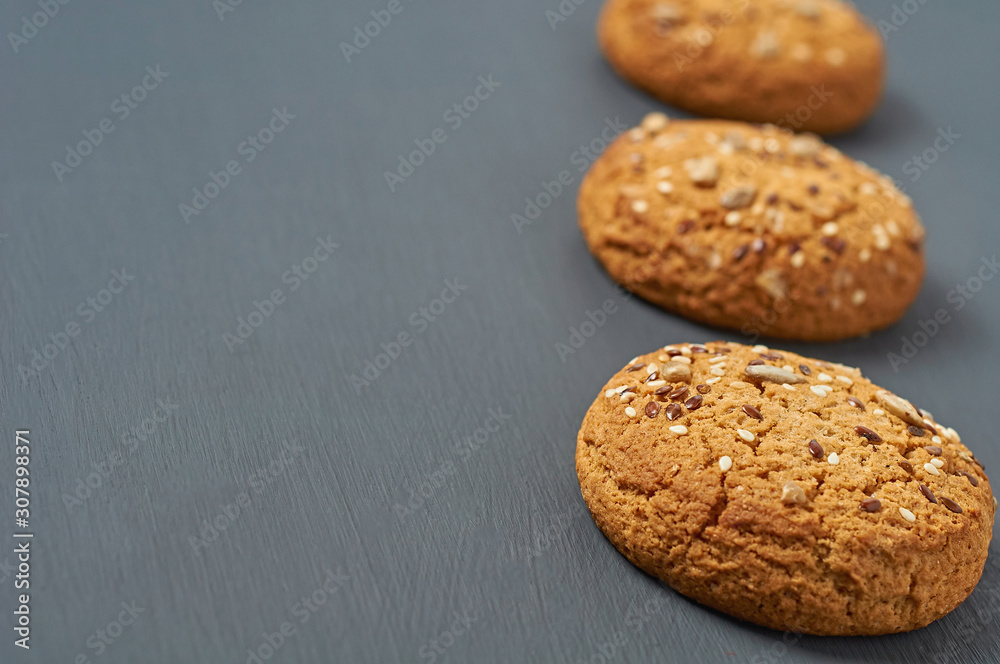 Row of three fresh homemade cookies with seeds of sunflower and sesame lies on dark scratched concrete table on kitchen. Space for text