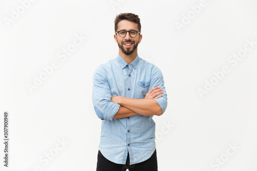 Happy laughing guy posing with arms folded. Handsome young man in casual shirt and glasses standing isolated over white background. Male portrait concept