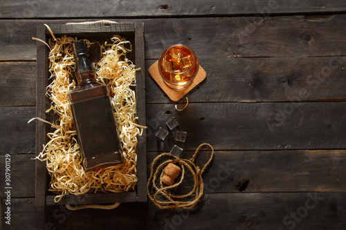 Whiskey with ice or brandy in a glass and a square carafe on an old wooden background. Whiskey with ice in a glass. Whiskey or cognac. Selective focus.