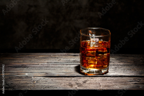 Whiskey with ice or brandy in a glass and a square carafe on an old wooden background. Whiskey with ice in a glass. Whiskey or cognac. Selective focus.