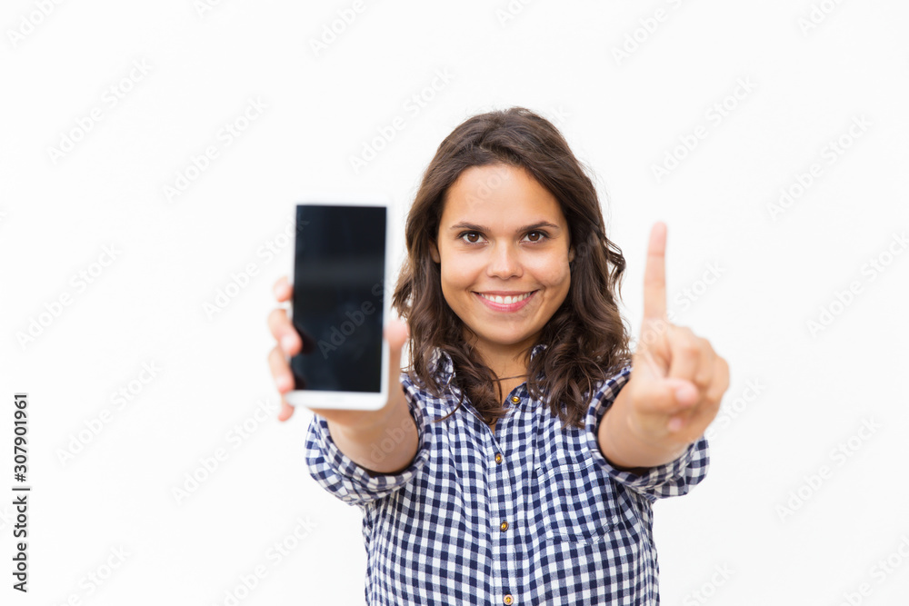 Joyful positive mobile phone user showing blank screen and index finger. Young woman in casual checked shirt standing isolated over white background. Advertising concept Joyful positive mobile phone user showing blank screen and index finger. Young woman in casual checked shirt standing isolated over white background. Advertising concept
