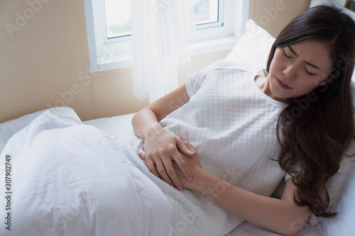 portrait of a woman lying on her bed touch stomach which pain