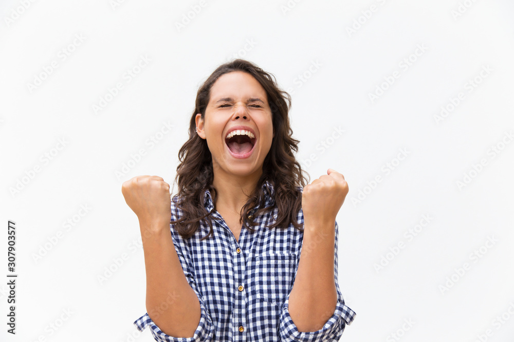 Joyful excited woman shouting for joy and making winner gesture. Young woman in casual checked shirt standing isolated over white background. Winning prize concept Joyful excited woman shouting for joy and making winner gesture. Young woman in casual checked shirt standing isolated over white background. Winning prize concept