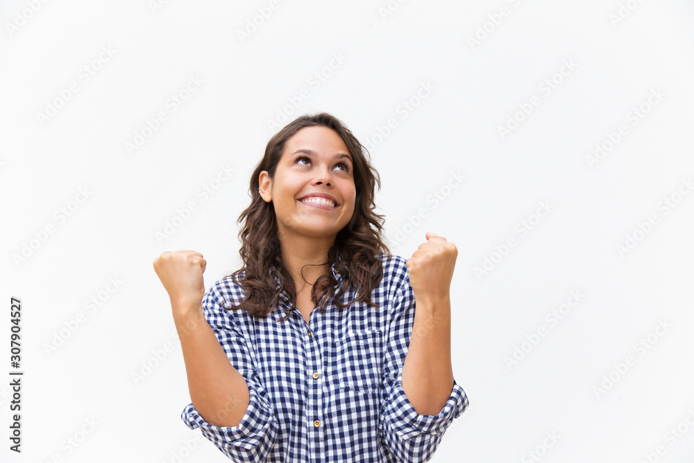 Cheerful happy woman making winner gesture and looking up at copy space. Young woman in casual checked shirt standing isolated over white background. Great news concept Cheerful happy woman making winner gesture and looking up at copy space. Young woman in casual checked shirt standing isolated over white background. Great news concept