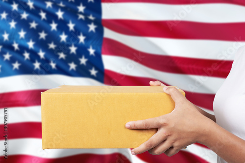 United States delivery service. International shipment theme. Woman courier hand holding brown box isolated on national flag background.