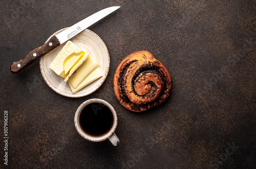 coffee and a bun with poppy seeds, butter and a knife on a stone background. breakfast concept with copy space for your text
