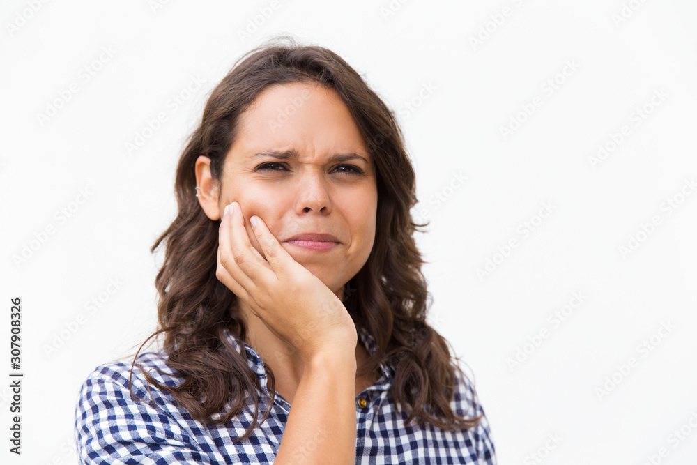 Closeup of stressed Latin woman holding cheek. Young woman in casual checked shirt standing isolated over white background. Thinking, or toothache concept Closeup of stressed Latin woman holding cheek. Young woman in casual checked shirt standing isolated over white background. Thinking, or toothache concept