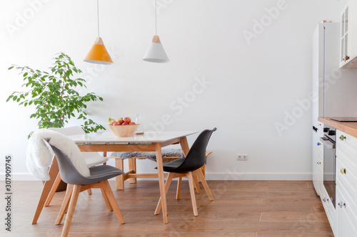 Modern interior of cozy kitchen, dining room, white furniture, lamps above wooden table, chairs, apples, bowl. Concept decor, design, advert, credit, mortgage, home for young family, magazine cover photo