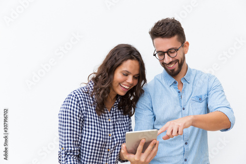 Cheerful couple watching content on tablet and laughing. Young woman in casual and man in glasses in glasses posing isolated over white background. Internet service concept