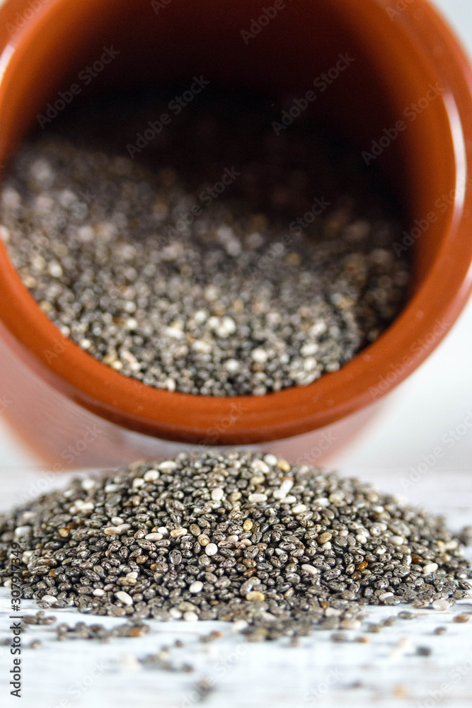 Edible seeds of chia, Salvia hispanica, a flowering plant of the mint family. A popular healthy food product. Chia seeds are poured from a brown clay pot. Blurred. Edible seeds of chia, Salvia hispanica, a flowering plant of the mint family. A popular healthy food product. Chia seeds are poured from a brown clay pot. Blurred.