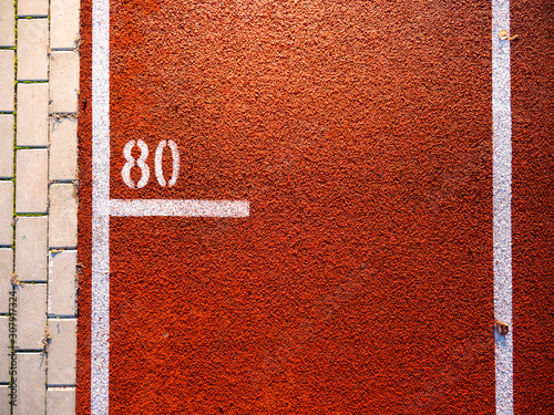 Shot from above of the red running track with the number 80. A piece of bricks from the pavement next to the track. photo