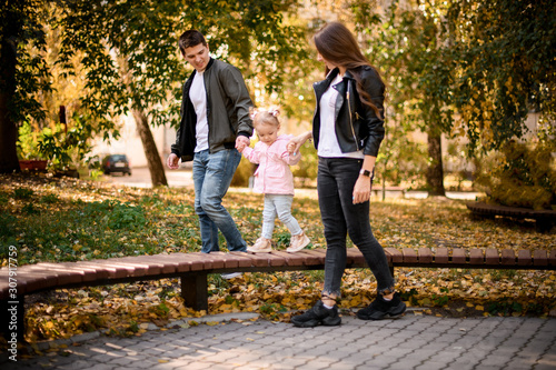 Mother and father holding their little daughter hand helping walking on the bench