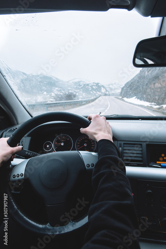 An unrecognizable person smokes while driving on a snowy road.
