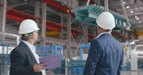 Construction engineers businessmen, teamwork meeting in plant facility. Two senior confident business people formal wear pointing to moving crane. investor businessman at modern factory