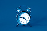 Alarm clock blue classic color in retro vintage style on blue background. Creative concept in minimal modern  style.