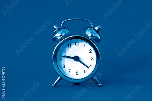 Alarm clock blue classic color in retro vintage style on blue background. Creative concept in minimal modern style.
