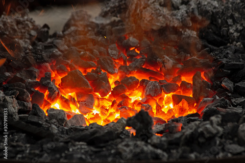 Flame and embers glow in a bonfire. Fire, heat, coal and ash with flying sparks.