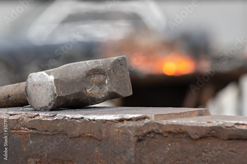 Old rusty hammer lies on the anvil with flame of brazier forge on background. Blacksmith, metalsmith, farrier tools.