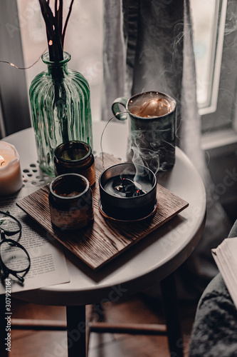 Cozy corner in the living room. Cozy warm blanket. Winter time. Candles on the table. Scandinavian interior decor. Cold winter time. Grey chair  throw blanket. Reading a book. Warm and cozy home