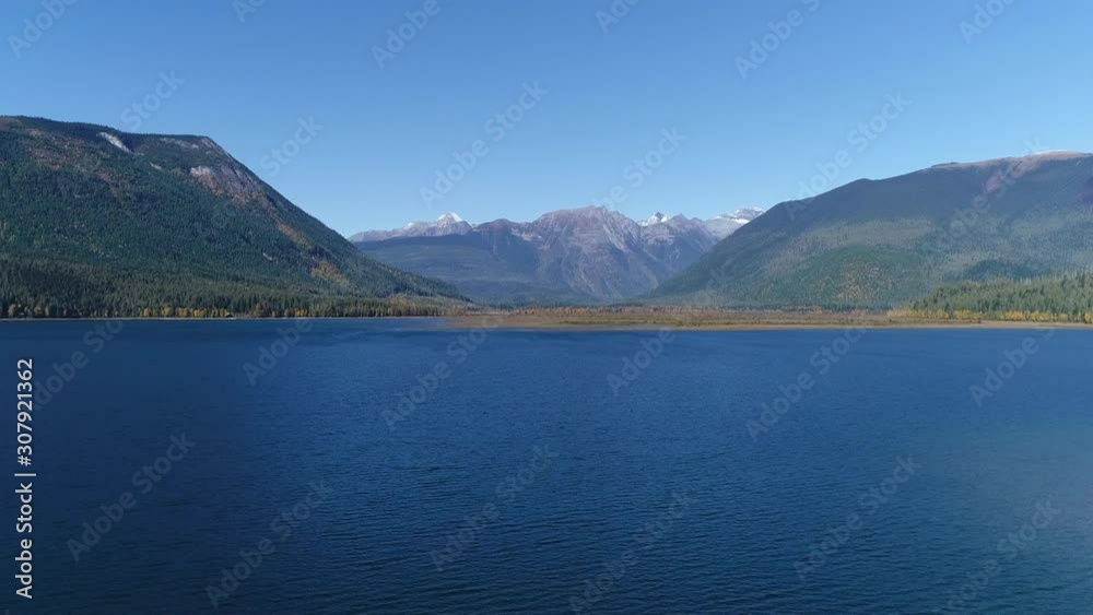 Drone, aerial, rising, wide shot of a lake with two hillsides framing a snowy mountain. Drone, aerial, rising, wide shot of a lake with two hillsides framing a snowy mountain.