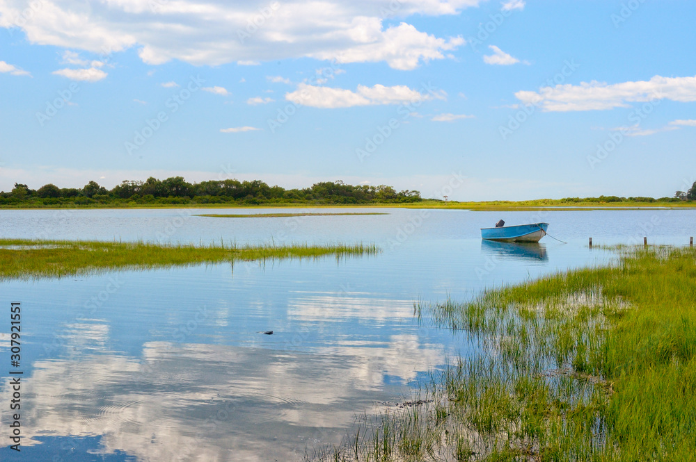 Tranquil view Niantic Connecticut salt marsh in summer with blue sky and blue boat reflections of cumulus clouds in still water with copy space, saltwater tidal marsh, East Lyme, New England scenic